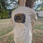 1 2 DOS - PredaColor Person seen from the back outdoors, wearing a light T-shirt with a large graphic that says 'Predacolor Gator Liner' and a yellow cap; palm trees and a fence in the background.