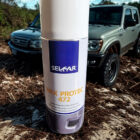 e8889d57-5fe7-4307-b1be-66c06f5b28f9 - PredaColor Close-up of a tall white cylindrical container labeled 'WAX PROTEC 472' in the foreground, with an off-road SUV in a dirt lot blurred in the background.