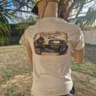 Back view of a person wearing a beige T-shirt with a large graphic of a vintage truck and 'Predacolor Gator Liner' lettering, outdoors under palm trees; yellow cap worn backwards.