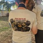 7 1 DOS - PredaColor Back view of a person in a beige T-shirt with a racing graphic on the back, standing beside a mannequin under a palm tree.