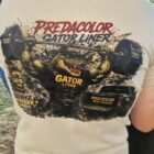 7 DOS - PredaColor Person wearing a beige T-shirt with a large graphic of a muddy alligator lifting a barbell and the words 'Predacolor' and 'Gator Liner' in red and yellow.