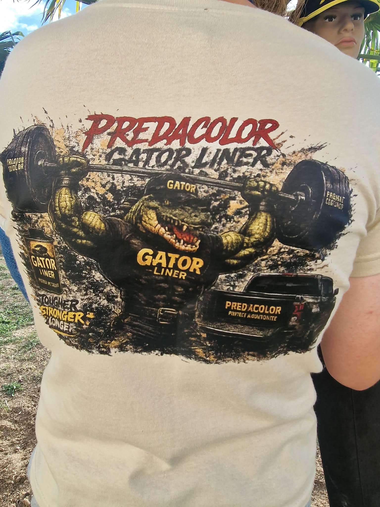 7 DOS - PredaColor Person wearing a beige T-shirt with a large graphic of a muddy alligator lifting a barbell and the words 'Predacolor' and 'Gator Liner' in red and yellow.
