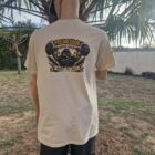 8 1 DOS - PredaColor Person standing with back to camera, wearing a beige graphic T-shirt and a yellow cap, outdoors near a palm tree.