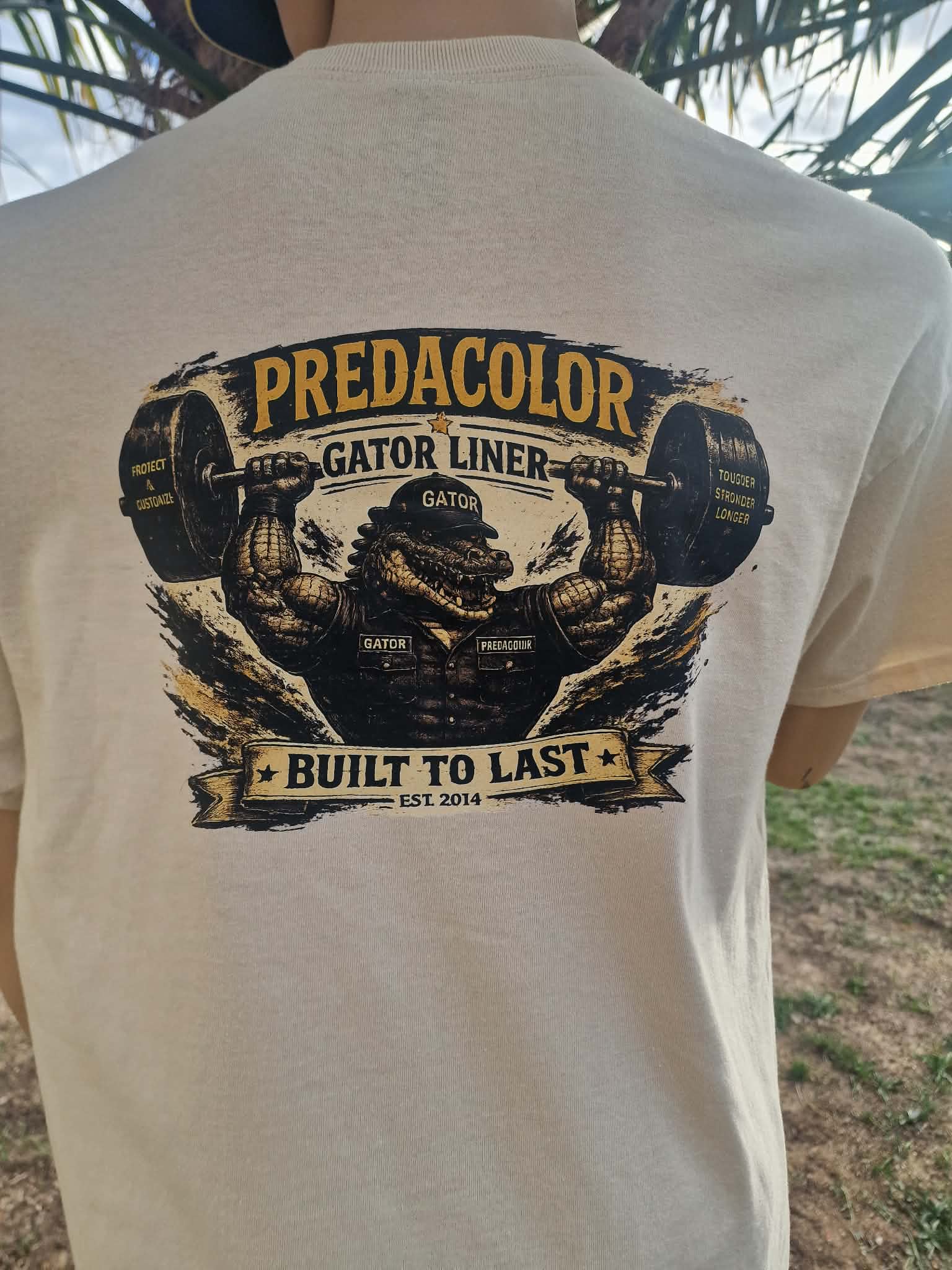 8 DOS - PredaColor Back of a beige T-shirt with a bold graphic of an alligator lifting a barbell and the text 'PREDACOLOR GATOR LINER BUILT TO LAST EST. 2014'